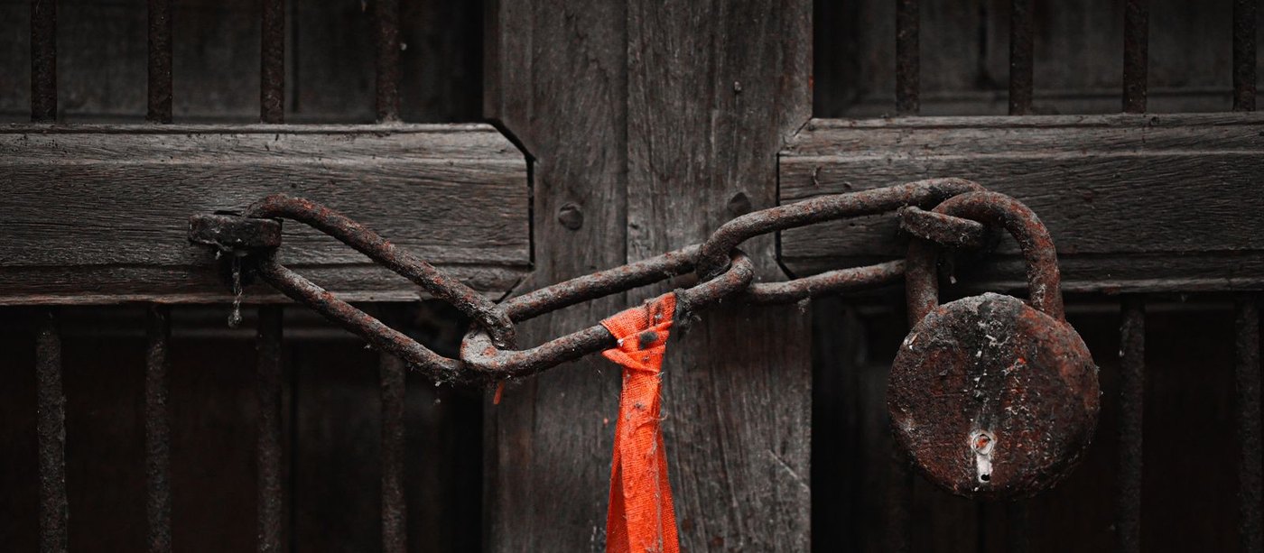 A heavily corroded padlock and rusted chain securing a weathered wooden gate
